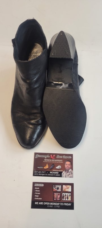 Repaired black leather dress boots beside the shop card